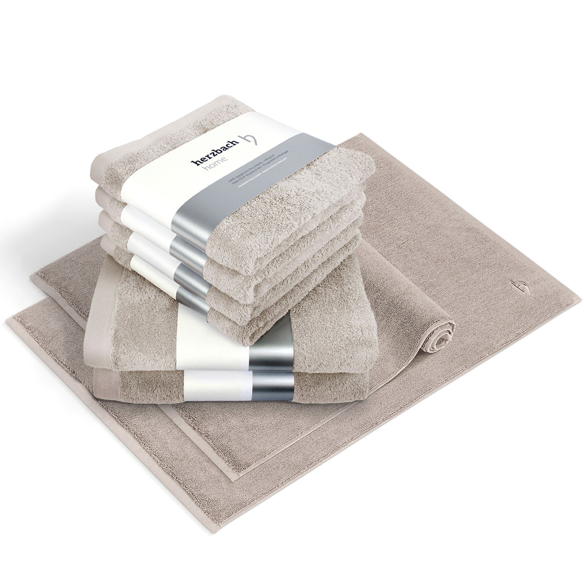 Pura Bundle Sandgrau – 6 gefaltete Handtücher mit herzbach home Banderole, ein flacher und ein aufgerollter Badvorleger im 2er-Set, weißer Hintergrund