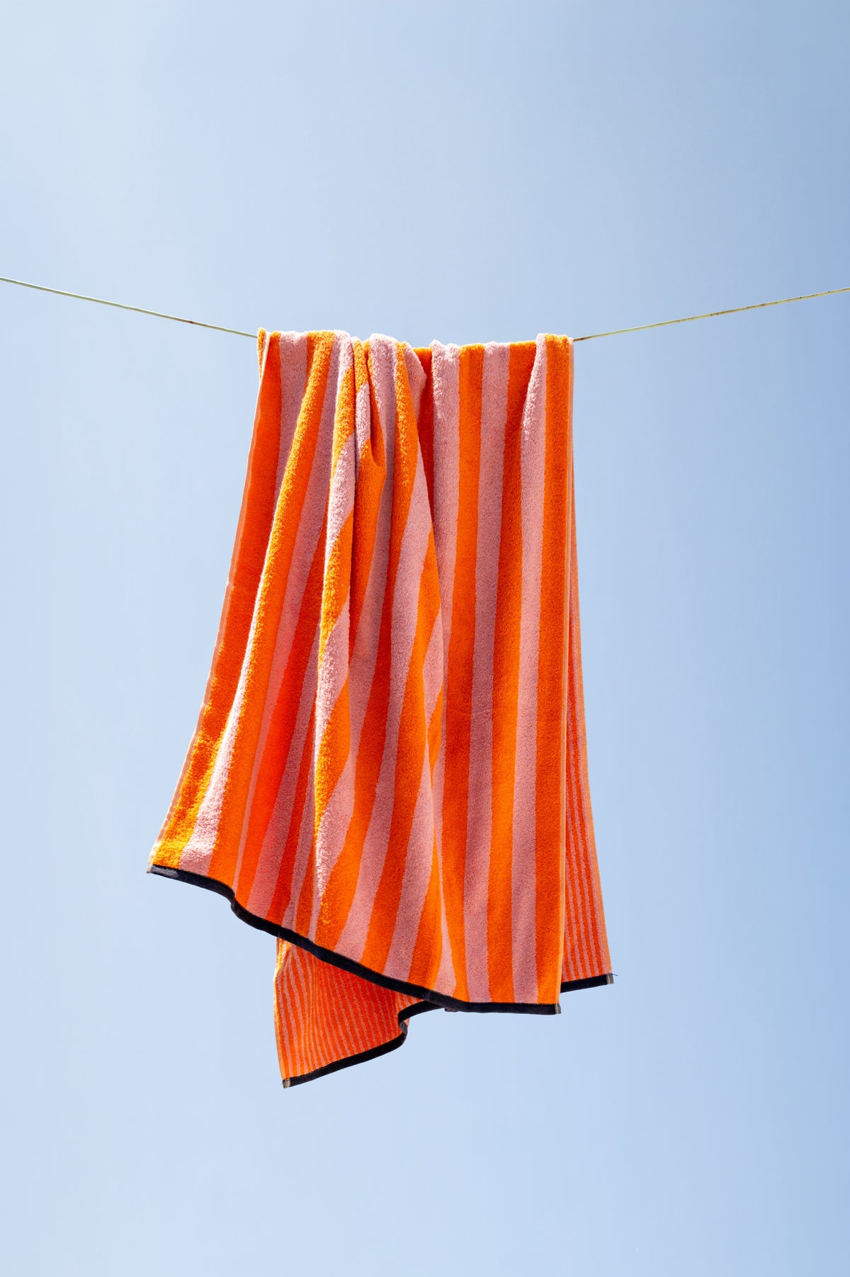 Duschtuch Good Vibes Mandarin Rosa auf der Wäscheleine – lässig drapiert vor blauem Sommerhimmel, leuchtende Streifen im Wind