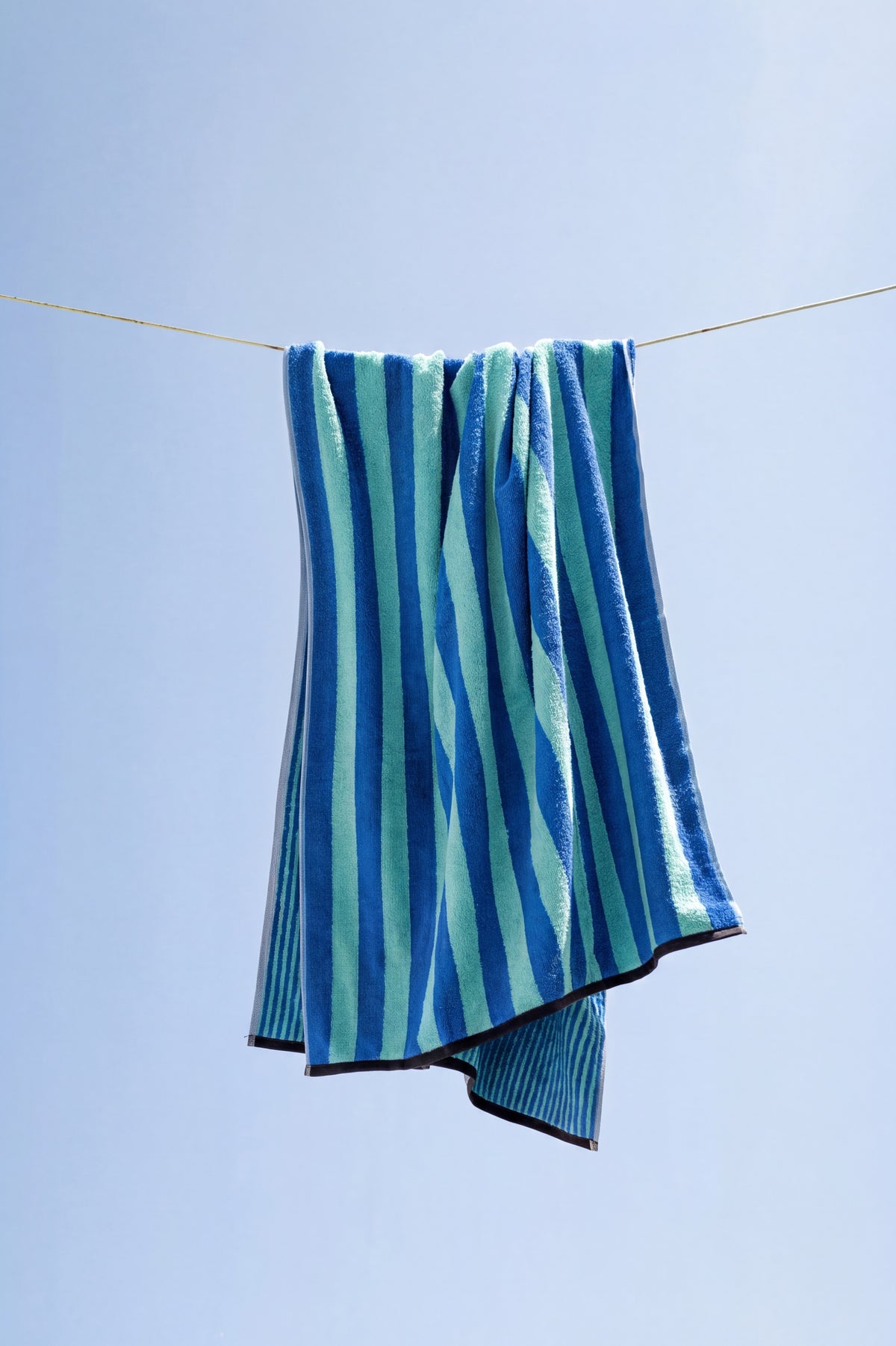 Duschtuch Good Vibes Türkis Blau auf der Wäscheleine – lässig drapiert vor blauem Sommerhimmel, Vorder- und Rückseite sichtbar