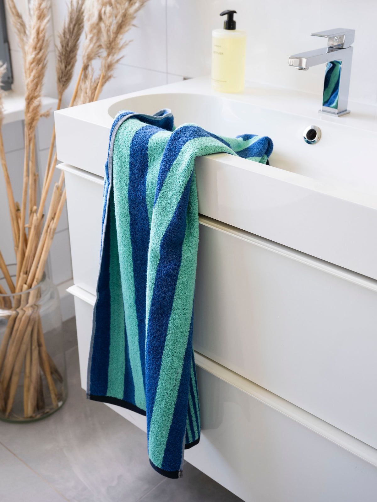 Badetuch Good Vibes Türkis Blau lässig über den Waschtisch drapiert – natürliches Badezimmer-Ambiente mit Pampasgras und Seifenspender