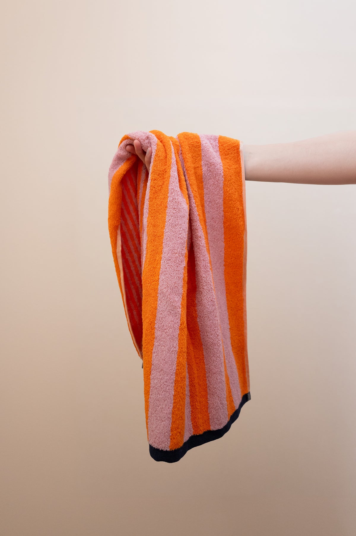 Hand hält das Handtuch Good Vibes Mandarin Rosa lässig – leuchtende Mandarin-Rosa-Streifen und weiche Frottee-Qualität im Detail