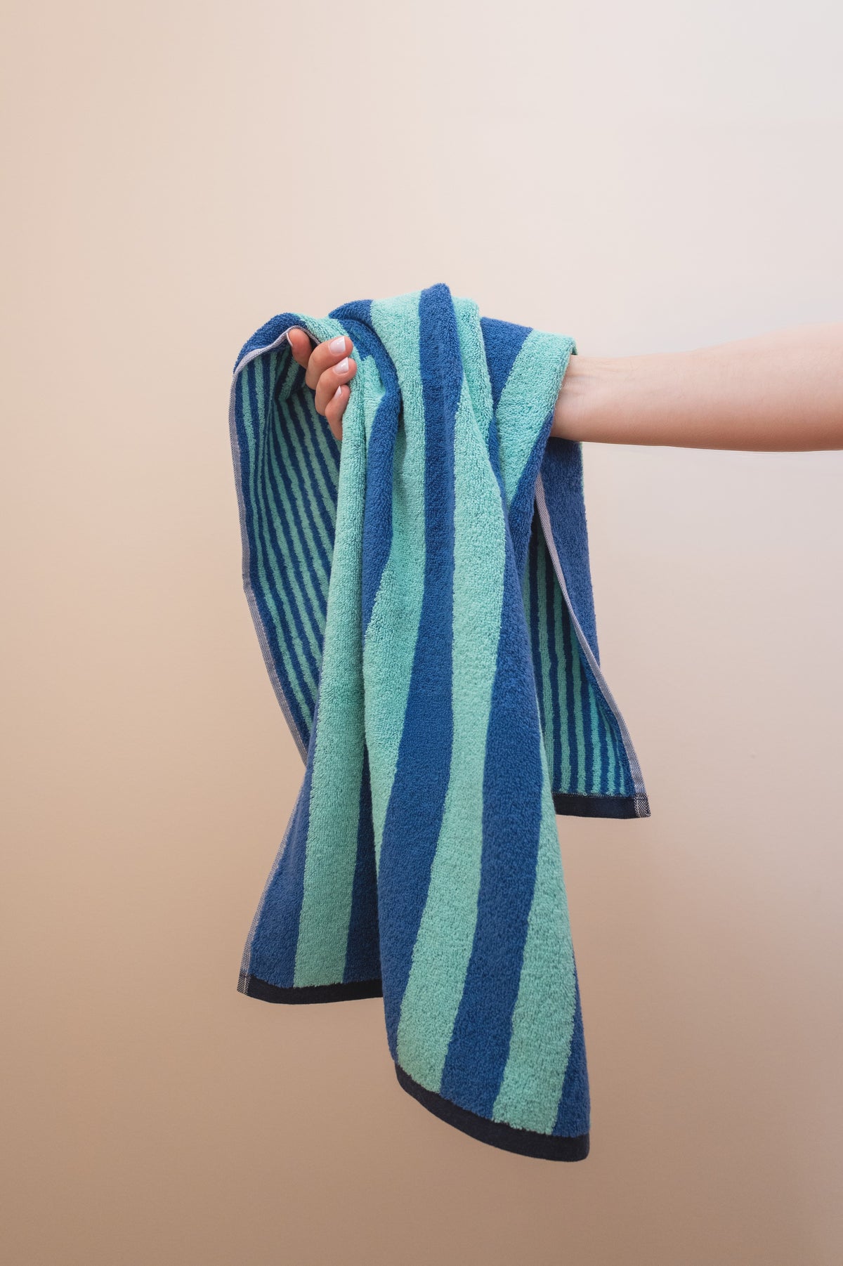 Hand hält das Handtuch Good Vibes Türkis Blau lässig – weiche Frottee-Qualität und lebendiges Streifenmuster im Detail