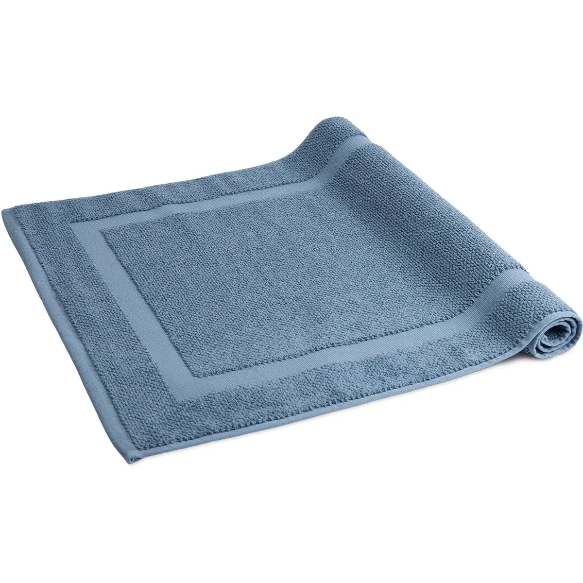 Spa Badvorleger Blau – einzelner Badvorleger von schräg oben, halb aufgerollt auf weißem Hintergrund, stahlblaues Baumwoll-Frottier mit charakteristischem Rahmendesign, 100% Baumwolle