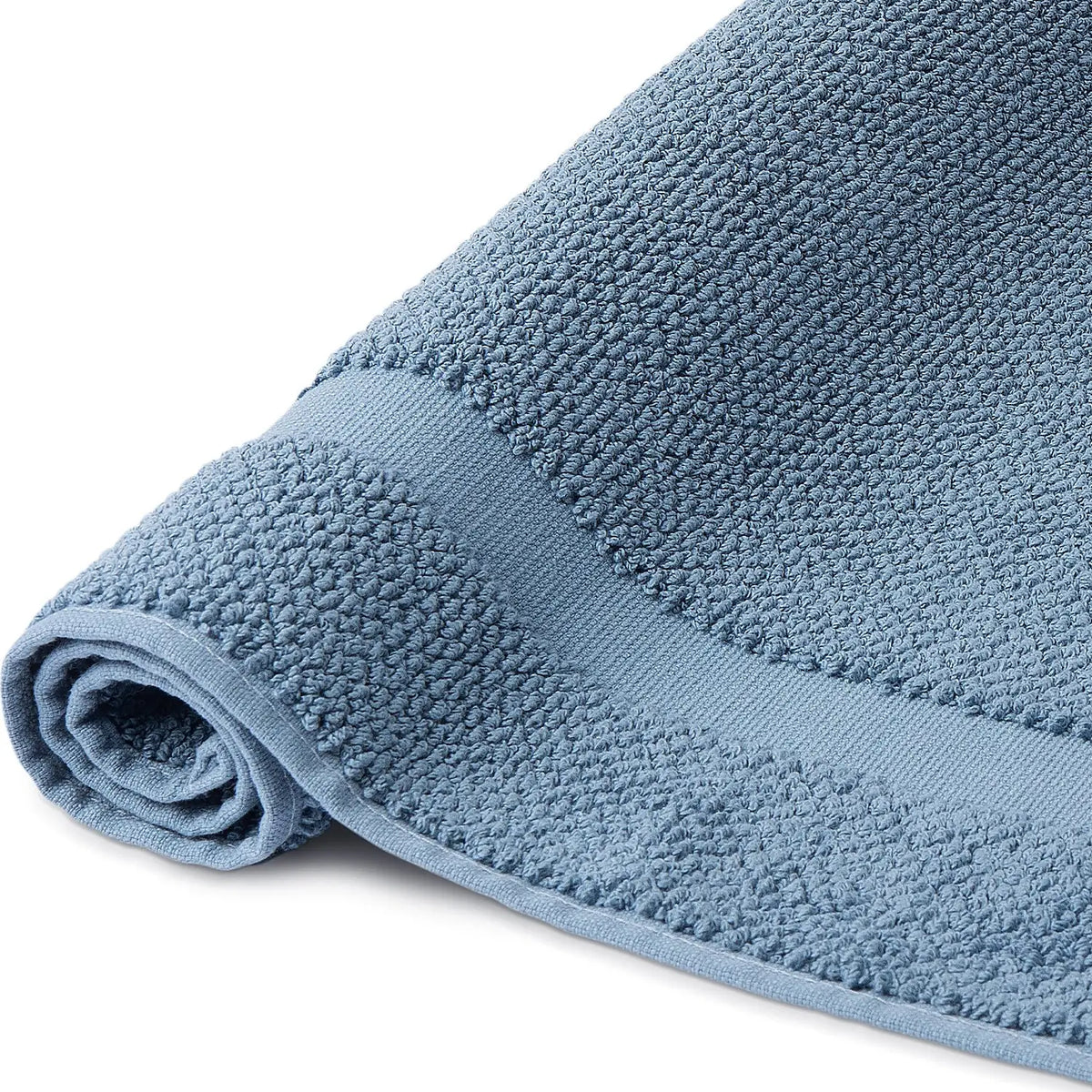 Spa Badvorleger Blau 2er Set – Nahaufnahme der Seite, aufgerollter Badvorleger mit grob strukturiertem Bouclé-Frottier und hellem Rahmenabschluss, kühler Stahlblauton, 100% Baumwolle