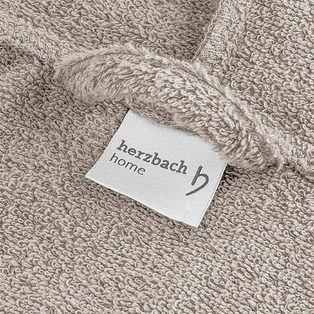 Nahaufnahme des sandgrauen Bademantelstoffs mit Herzbach Home Etikett