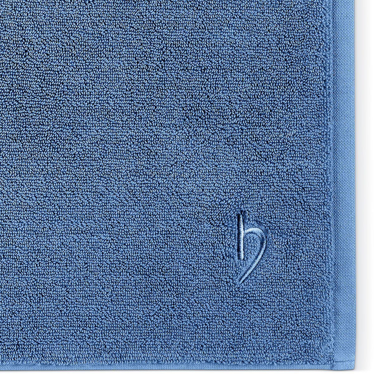 Pura Badvorleger Blau – Nahaufnahme der Ecke mit dichter Frottier-Struktur und Ton-in-Ton herzbach home Logostickerei auf stahlblauem Untergrund