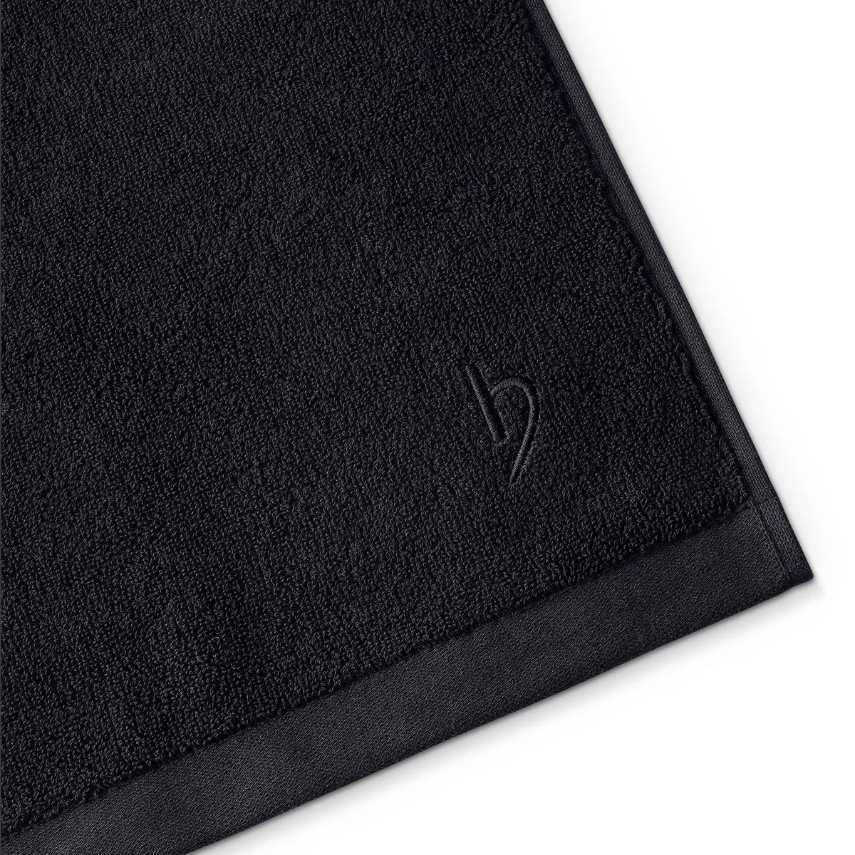 Duschtuch Deep Black – Eckendetail mit eingesticktem herzbach home Logo und feinem Satin-Saum in Schrägansicht