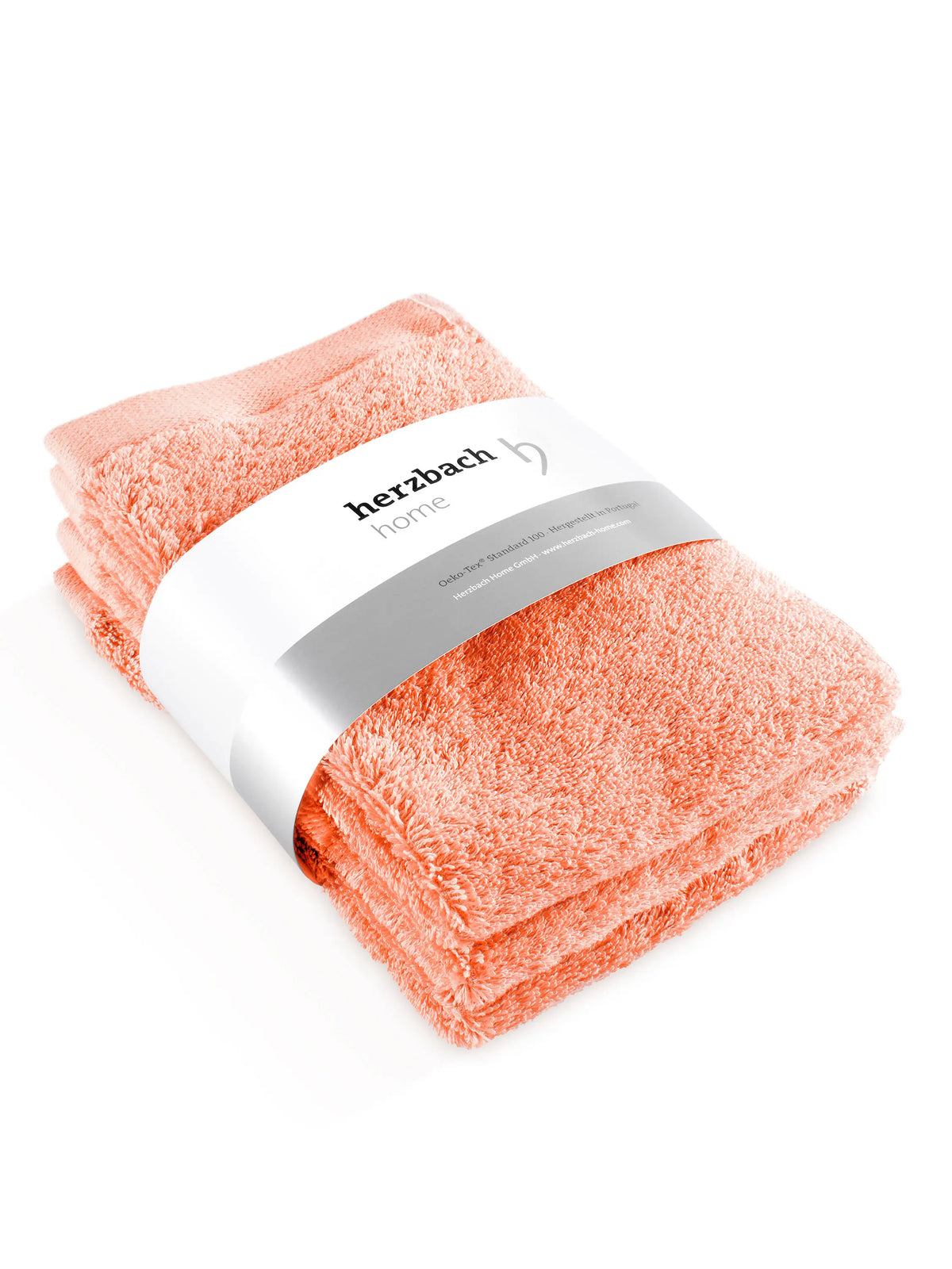 Drei gefaltete Pura Gästehandtücher in Coral mit Herzbach Home Papierbanderole