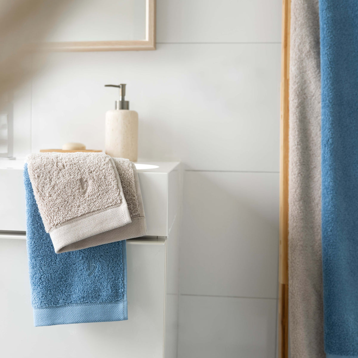 Blaues und sandgraues Pura Tuch im Badezimmer am Waschbecken aufgehängt