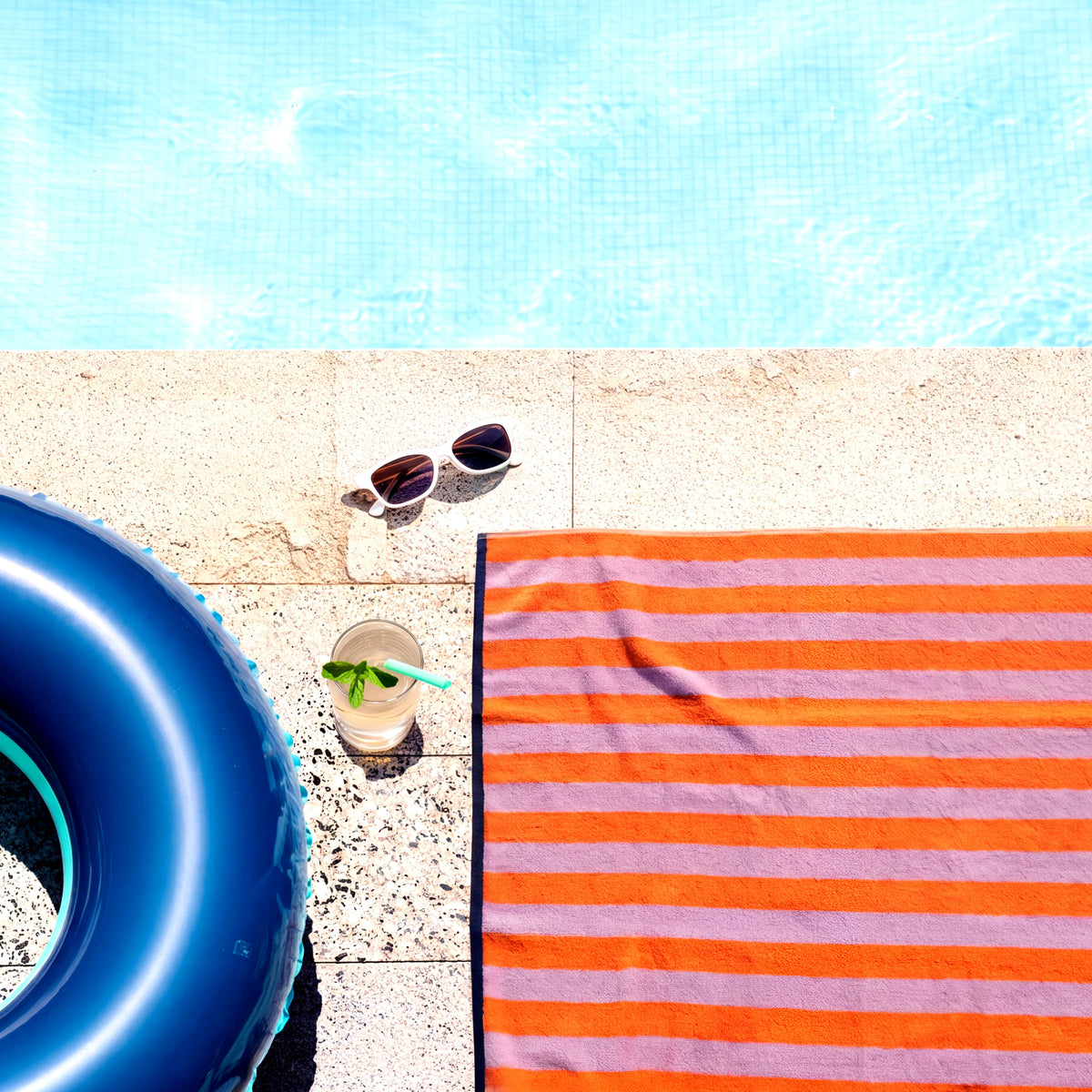 Duschtuch Good Vibes Mandarin Rosa am Poolrand ausgebreitet – Sommerfeeling von oben mit Schwimmring, Sonnenbrille und Erfrischungsgetränk