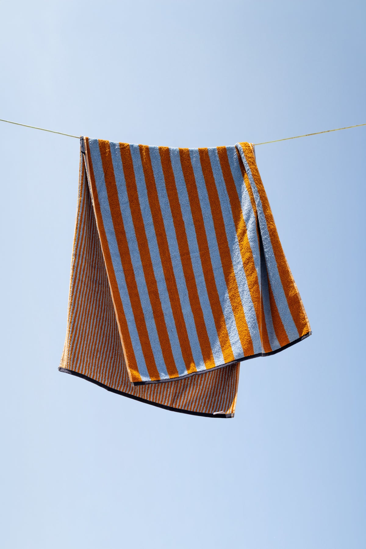 Badetuch Good Vibes Caramel Hellblau auf der Wäscheleine – lässig drapiert vor blauem Sommerhimmel, Vorder- und Rückseite sichtbar