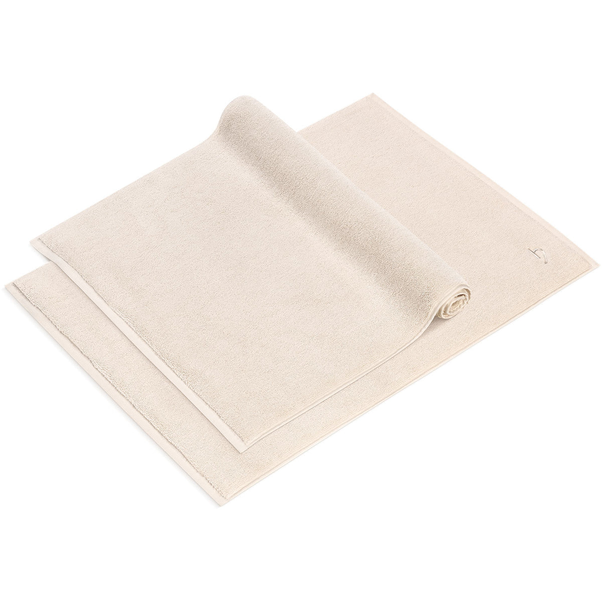 Pura Badvorleger 2er Set Creme – ein ausgebreiteter und ein gerollter Badvorleger 50x70 cm von schräg oben, flauschiges Frottier mit feingemusterter Bordüre und Ton-in-Ton-Logostickerei, 100% Baumwolle 1200 g/m²