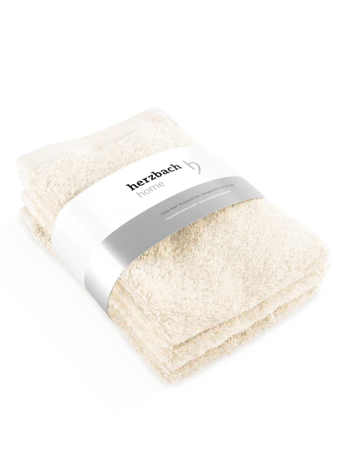Drei gefaltete cremefarbene Pura Gästehandtücher mit Herzbach Home Papierbanderole
