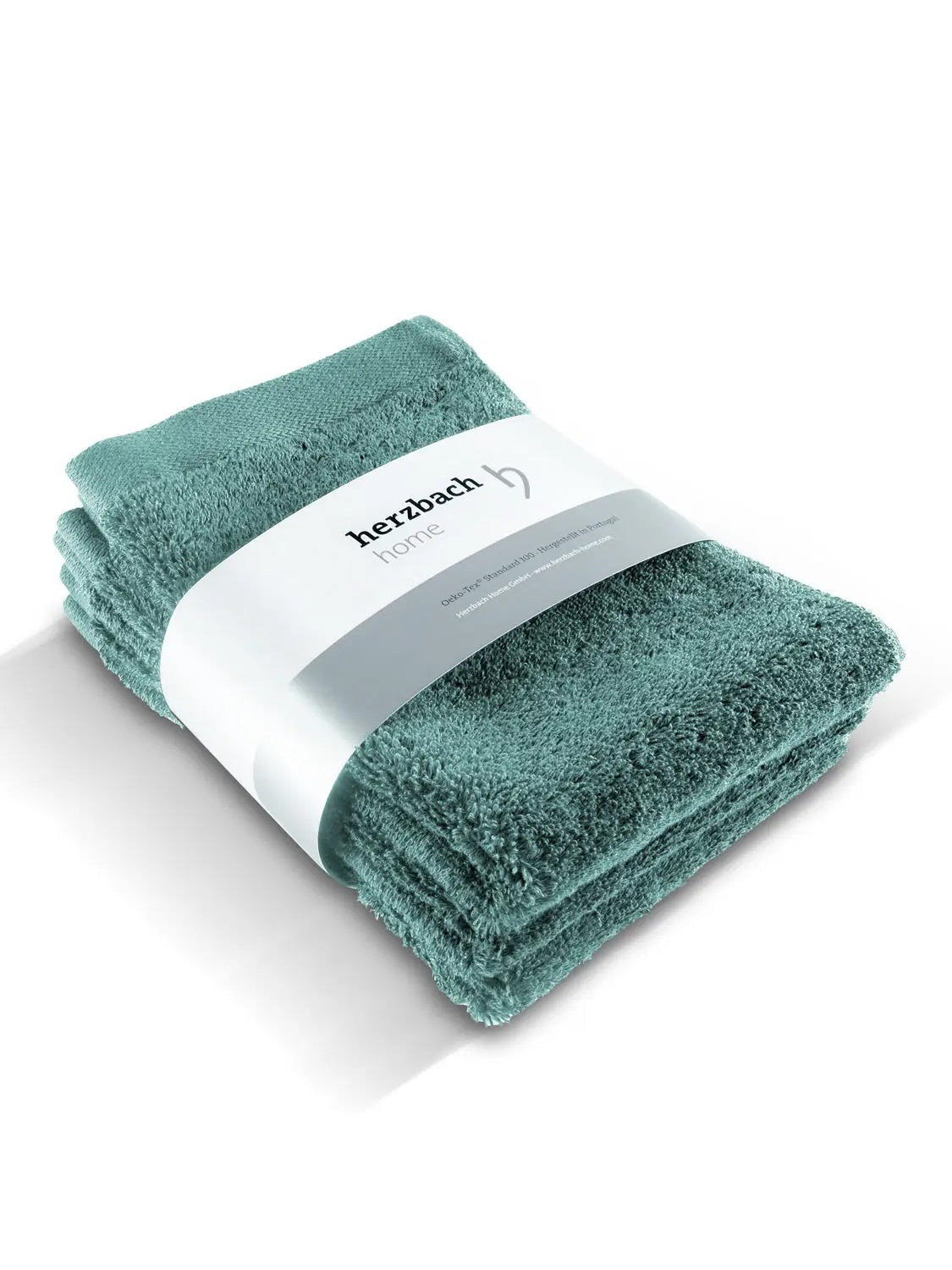 Pura Gästehandtuch 3er-Set Ozeangrün – drei gestapelte Gästehandtücher mit herzbach home Banderole in Schrägansicht auf weißem Hintergrund, voluminöse Frottier-Qualität