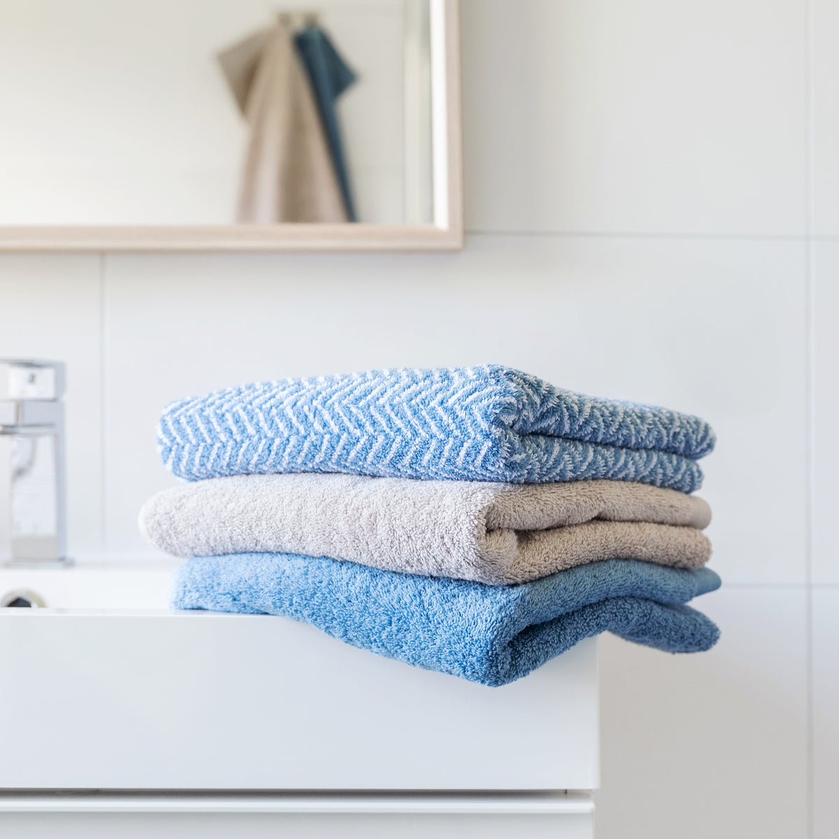 Gefaltete Handtücher in Blau und weiteren Farben auf einem weißen Waschtisch