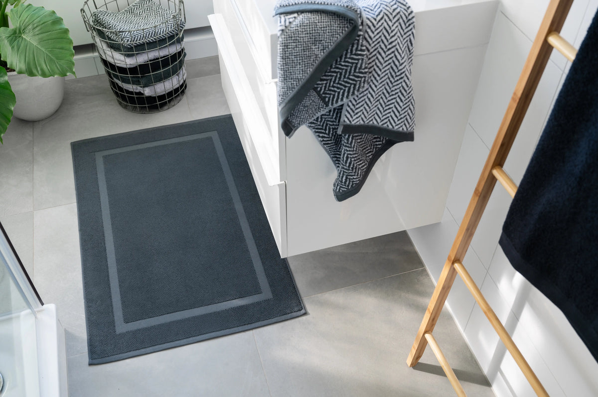 Spa Badvorleger Anthrazit – Lifestyle-Vogelperspektive im modernen weißen Badezimmer vor Waschtisch, anthrazitfarbener Badvorleger mit Rahmendesign, Bambusleiter mit dunklen Handtüchern, Drahtwäschekorb und große Zimmerpflanze